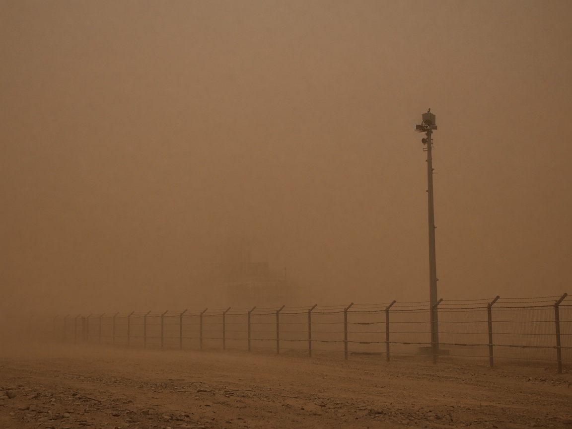 Dust haze hiding an oilfield fence and a camera pole